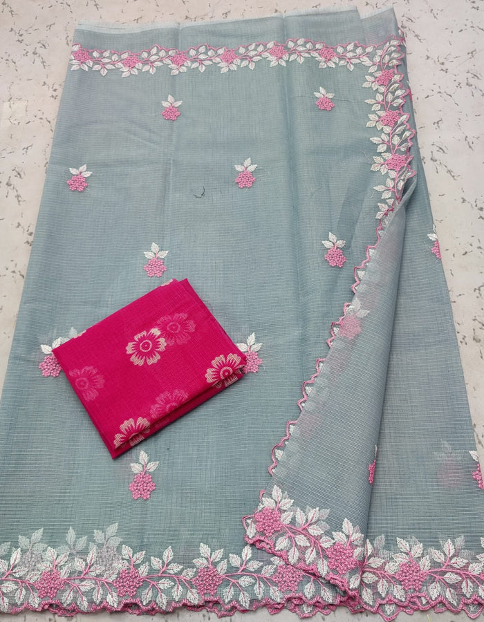 A folded grey-colored cotton saree with embroidered floral patterns and a pink contrasting blouse piece with floral hand block print.