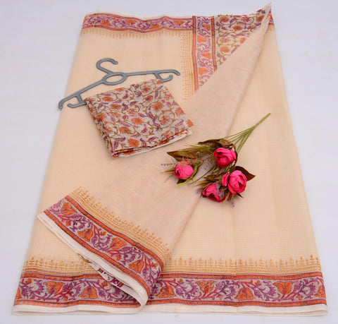 A cream-colored Kota cotton saree with block print design, displayed with its unstitched blouse and a small branch of flowers, adding a decorative touch.