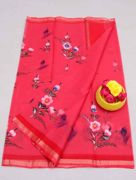 A red-colored pure cotton Kota hand-painted saree displayed alongside a floral design brush, with an attached running unstitched blouse piece.