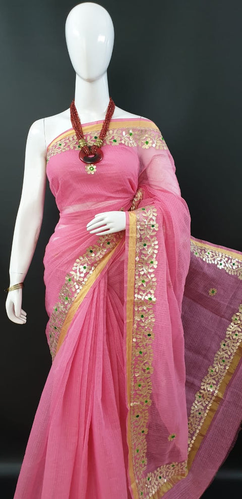  A pink Kota Doria saree with intricate gota patti work, displayed on a mannequin, paired with a red statement necklace.