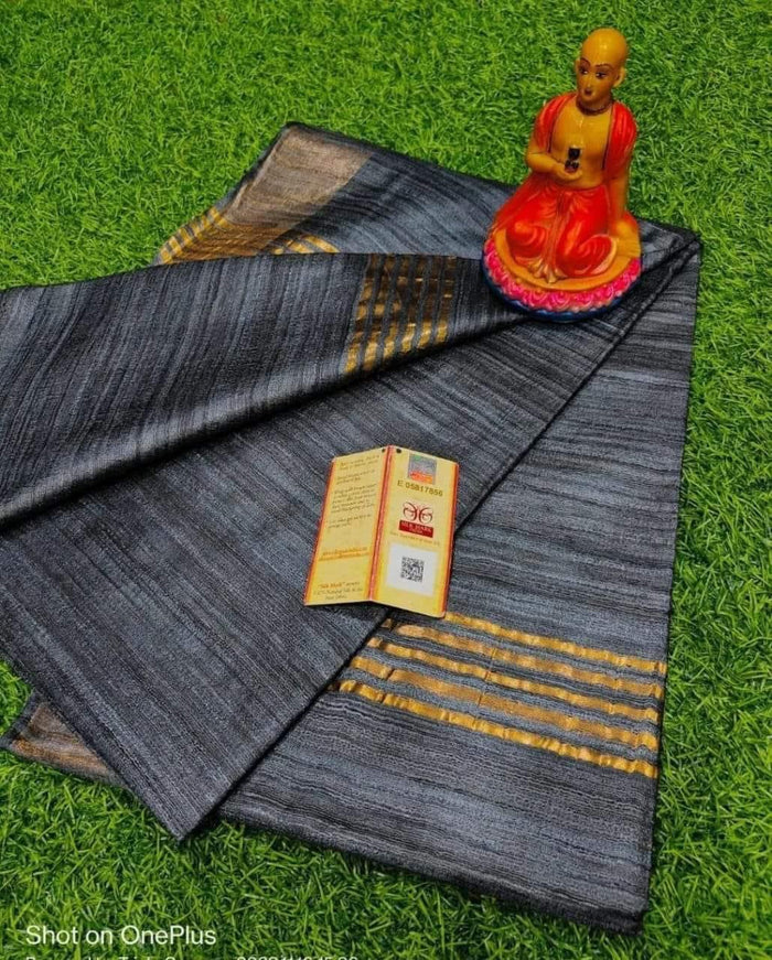 Gray fabric with gold stripes on a green grass background, featuring a small statue and a tag.