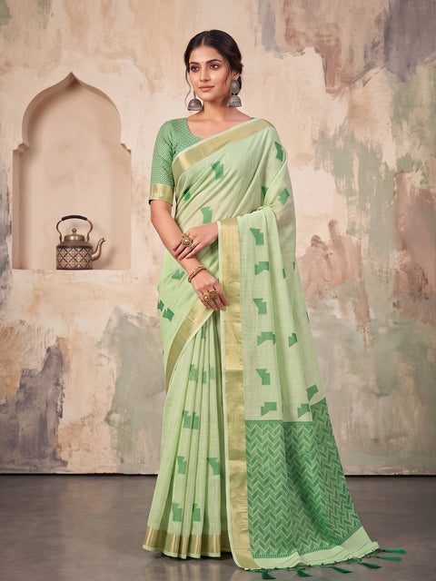A woman models a light green saree with a matching green and gold printed blouse. The saree features a light green body with green motifs, a wide gold border, and a contrasting green patterned pallu.